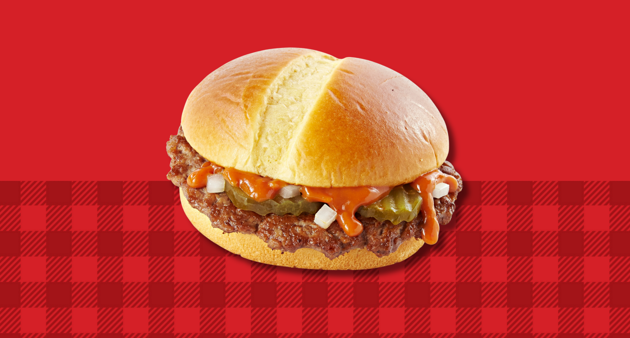 Jack’s cheeseburger with pickles, onions and sauce on a toasted bun against a red checkered background.