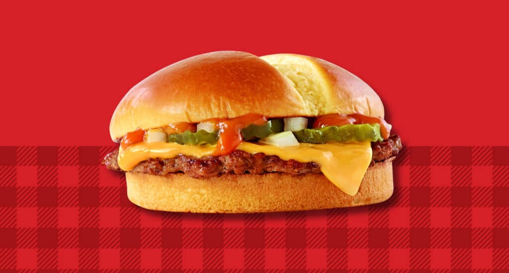 A Jack’s cheeseburger topped with American cheese, pickles, onions and signature sauce on a toasted bun, set against a red background with a red gingham pattern.