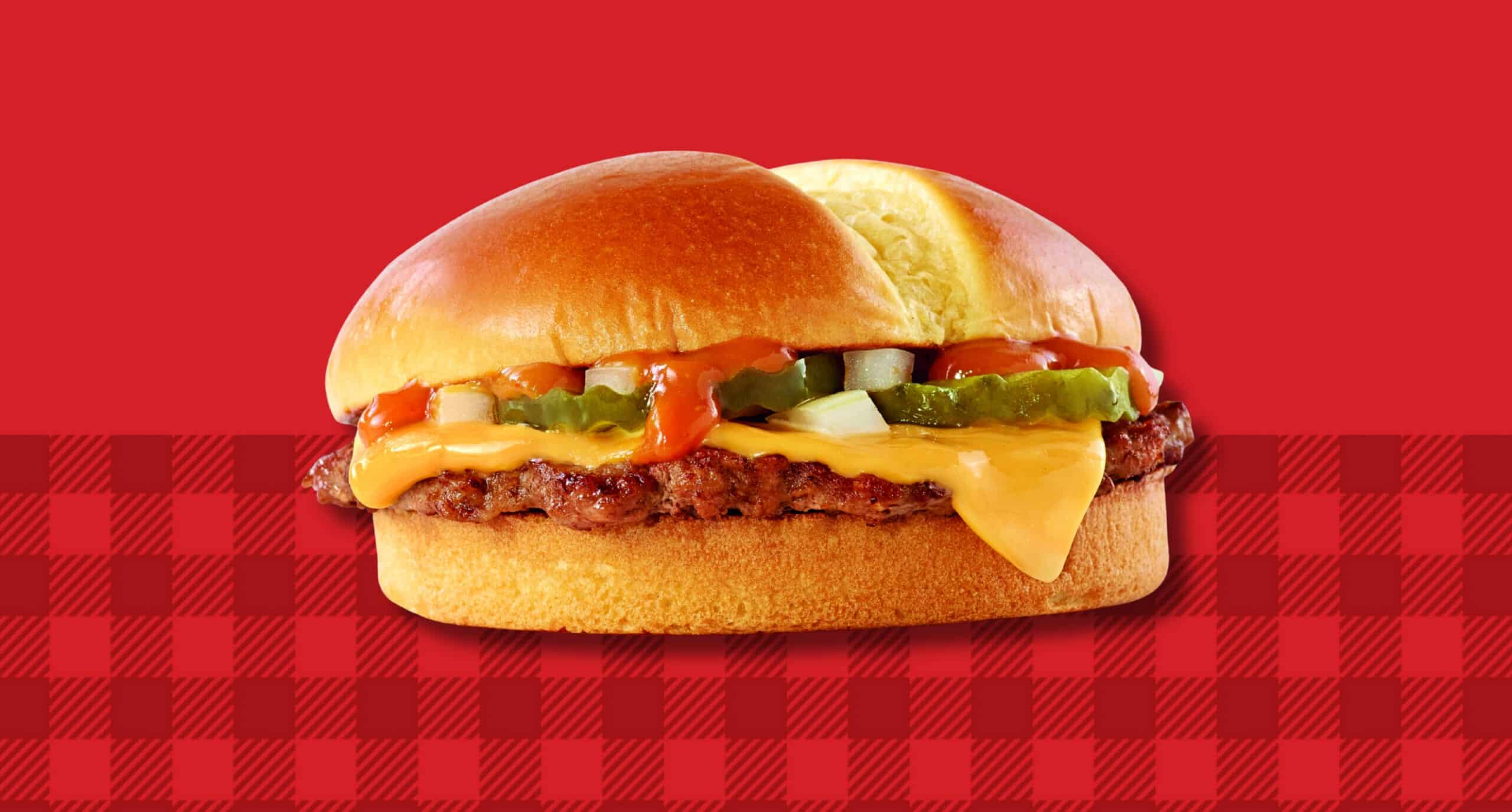 A Jack’s cheeseburger topped with American cheese, pickles, onions and signature sauce on a toasted bun, set against a red background with a red gingham pattern.